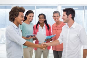 Attractive businessmen shaking hands at work in front of coworkers