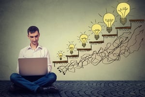 Happy young man entrepreneur working on computer sitting on a floor in his office successful in increasing internet website traffic. Promotion, company growth concept. Isolated on gray wall background